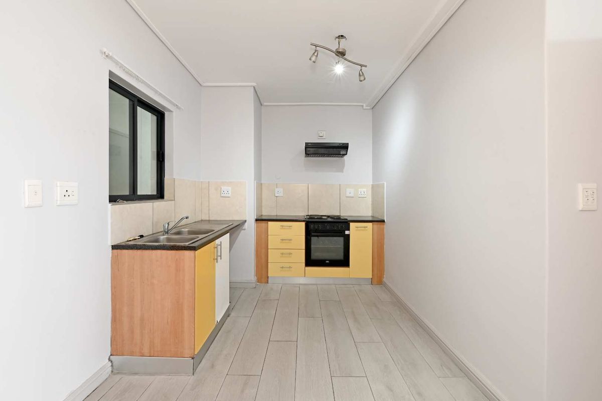 A functional kitchen featuring light wood cabinetry, dark countertops, a built-in oven, hob, and extractor fan with tiled splashbacks and light-toned flooring.