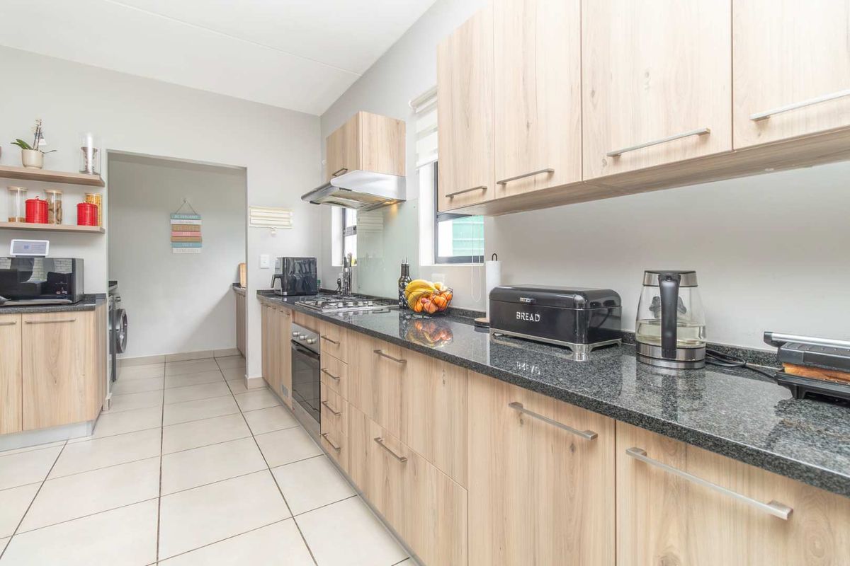 Modern kitchen featuring light wood cabinetry, granite countertops, built-in oven, gas hob, and stainless steel extractor fan, with an adjacent laundry area.