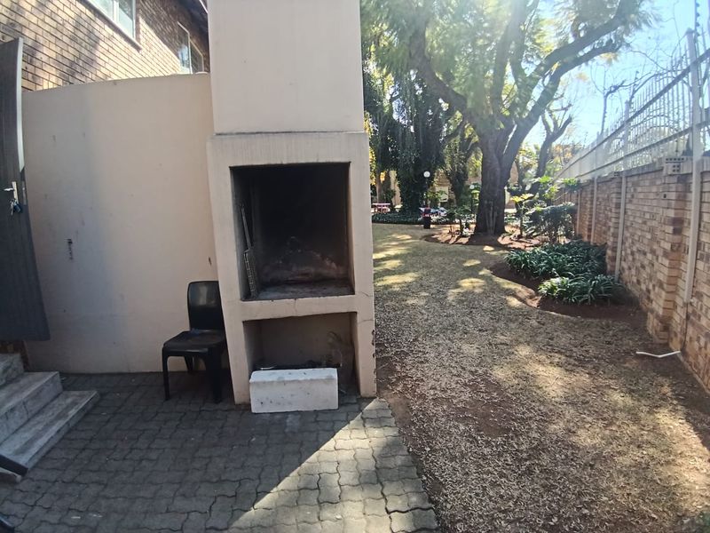 Rear garden area featuring a paved patio with a built-in braai, brick boundary walls, and established trees.