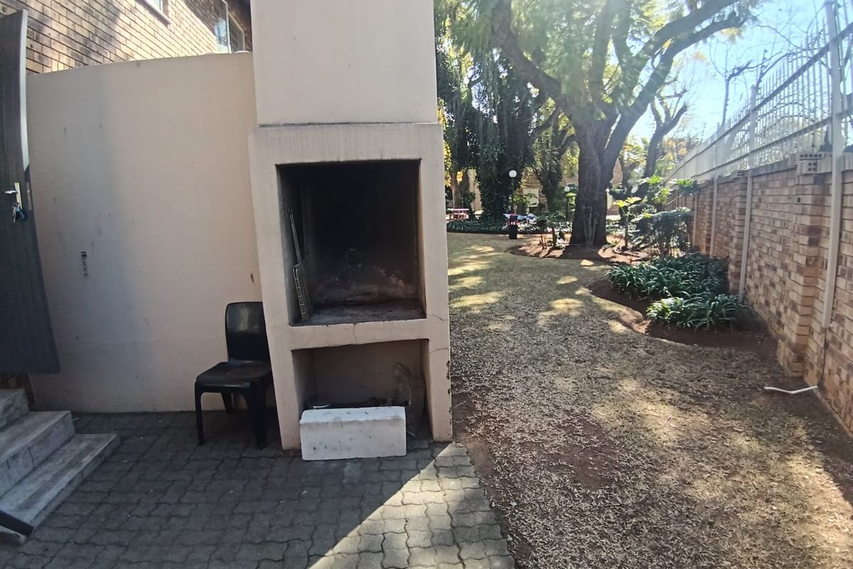Rear garden area featuring a paved patio with a built-in braai, brick boundary walls, and established trees.