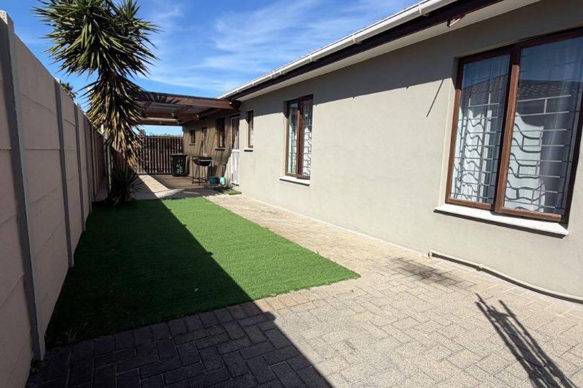 Rear exterior view featuring a paved patio area, artificial lawn, and a timber pergola structure along the side of the house.