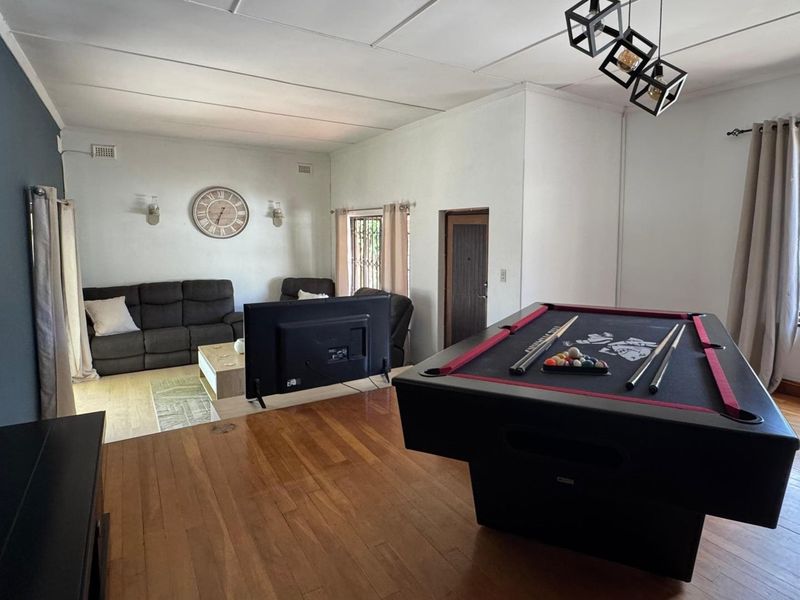Spacious living area featuring hardwood flooring, security bars on windows, and modern pendant lighting, currently configured as a combined lounge and games room.
