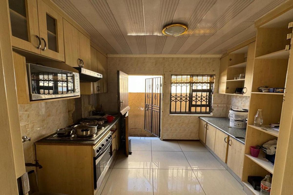 A functional kitchen featuring built-in cabinetry, a built-in oven with hob, and direct access to an outdoor area through a security gate.