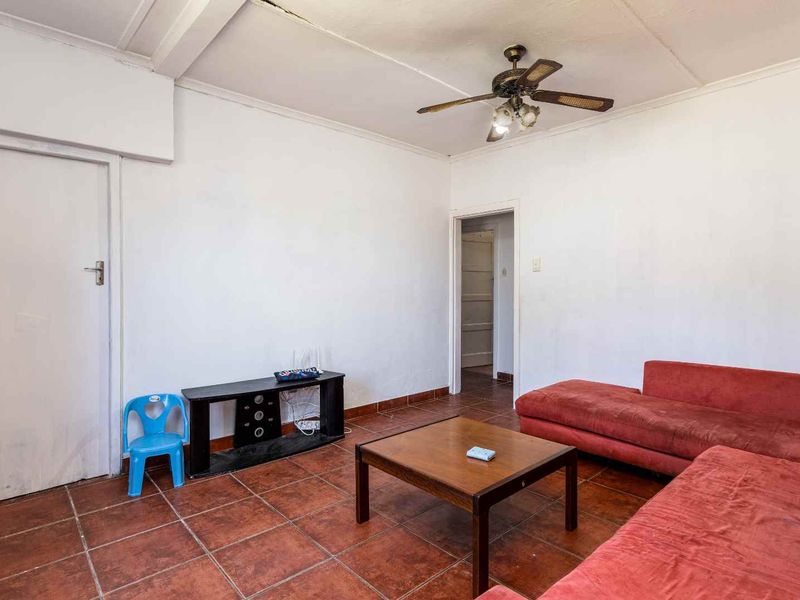 A living room featuring tiled flooring and a ceiling fan, requiring cosmetic updates to the walls and ceiling to improve its overall condition.
