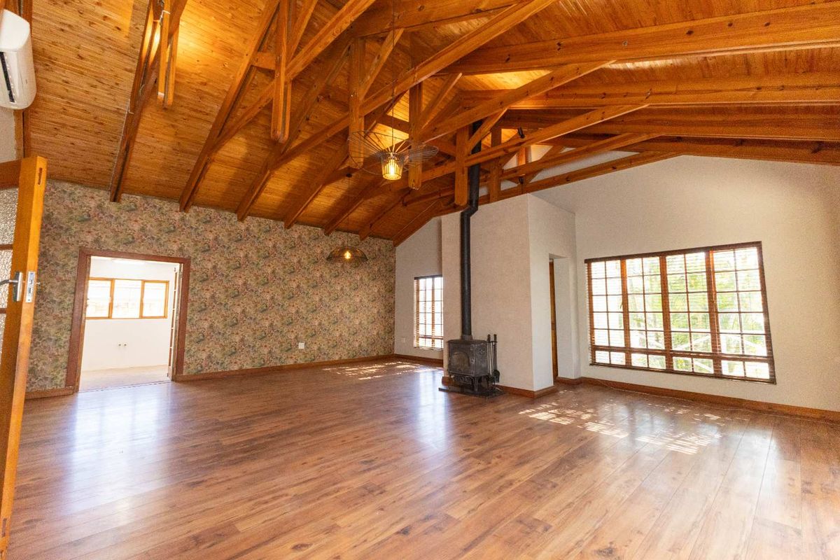 Spacious living area featuring high vaulted timber ceilings, exposed wooden trusses, a cast-iron fireplace, and large windows providing ample natural light.