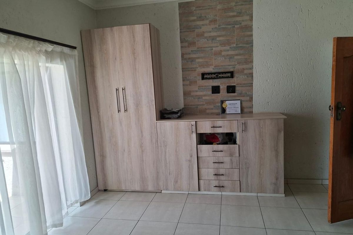 A bedroom featuring built-in light wood cabinetry, tiled flooring, and a decorative stone-tiled feature wall section.
