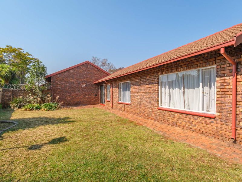 Rear view of the townhouse featuring a face brick facade, tiled roof, paved walkway, and a private garden area with security fencing.