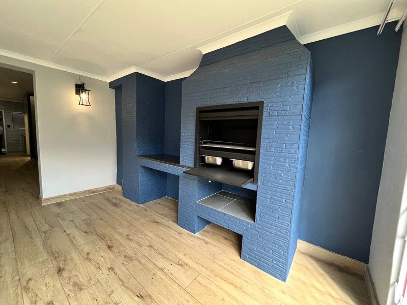 A clean, covered patio area featuring a built-in braai, modern laminate flooring, and a contemporary blue painted brick finish.