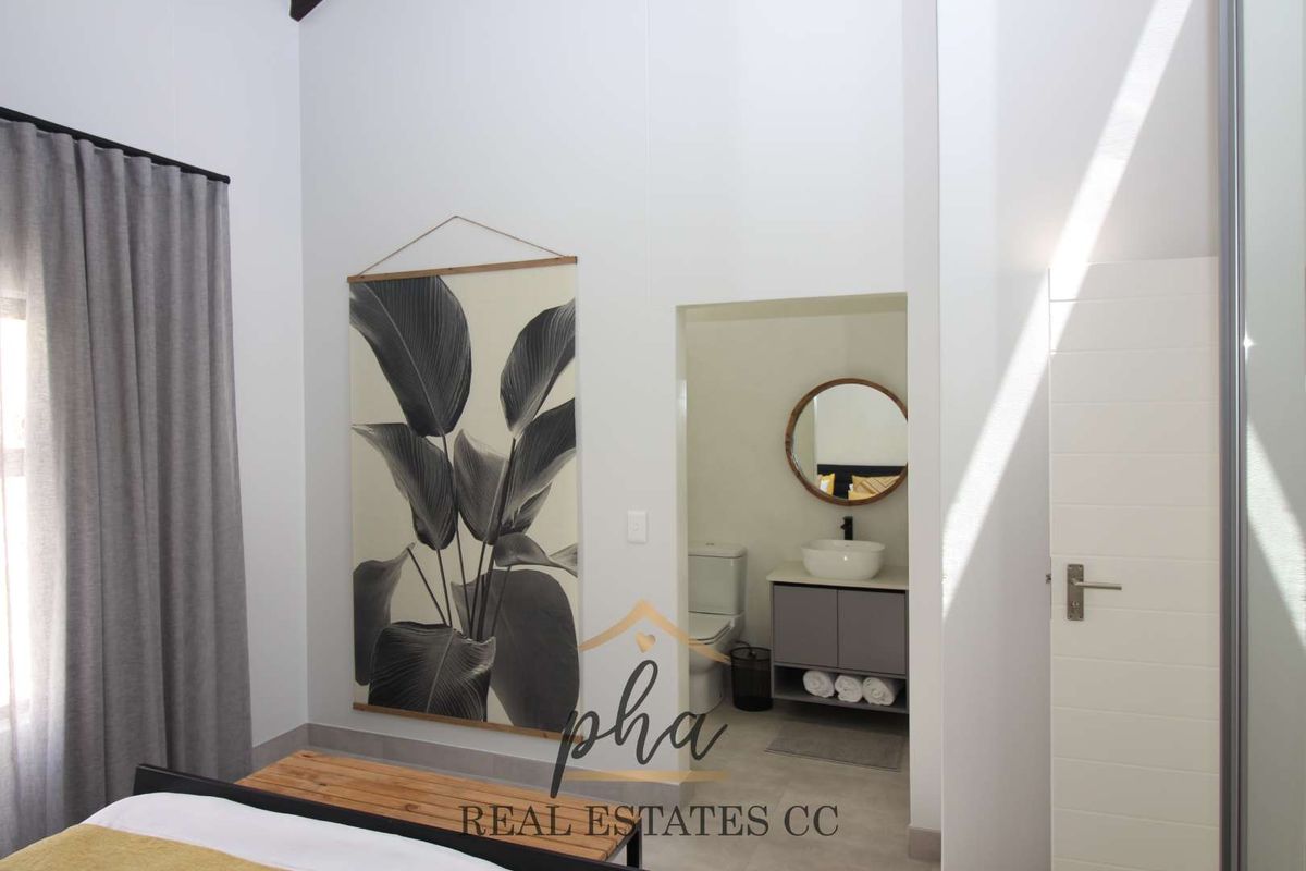 A bright bedroom featuring high ceilings and an en-suite bathroom with a modern vanity, vessel sink, and toilet.