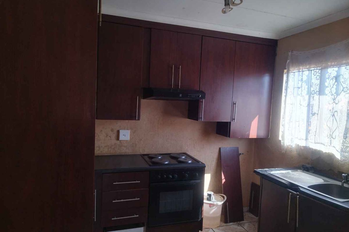 A functional kitchen featuring dark wood cabinetry, a built-in oven with hob, extractor fan, and a stainless steel sink.
