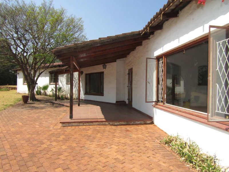 A rear view of the house featuring a covered patio with terracotta tiling, timber beams, and brick paving leading out to the garden.