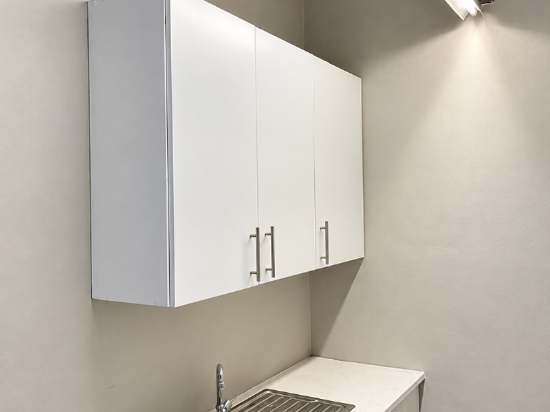 A functional utility or scullery area featuring white built-in cabinetry, a stainless steel sink, and a clean countertop workspace.