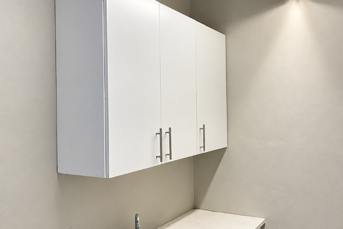 A functional utility or scullery area featuring white built-in cabinetry, a stainless steel sink, and a clean countertop workspace.