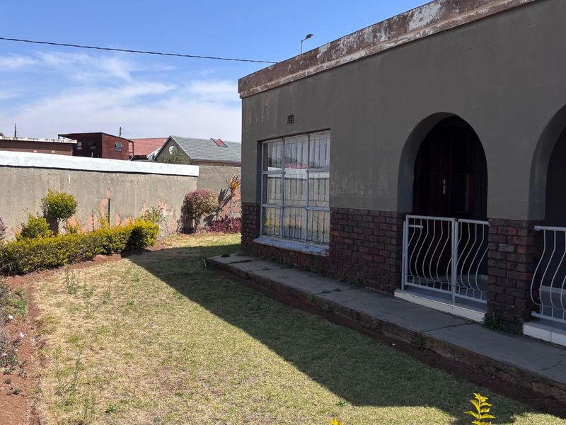 Rear exterior view of the house featuring a brick and plaster facade, arched entrance, security bars, and a private garden area with perimeter wall.