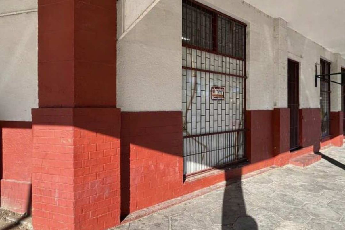 Exterior view of a commercial building facade featuring a covered walkway, brick detailing, and security-barred windows.