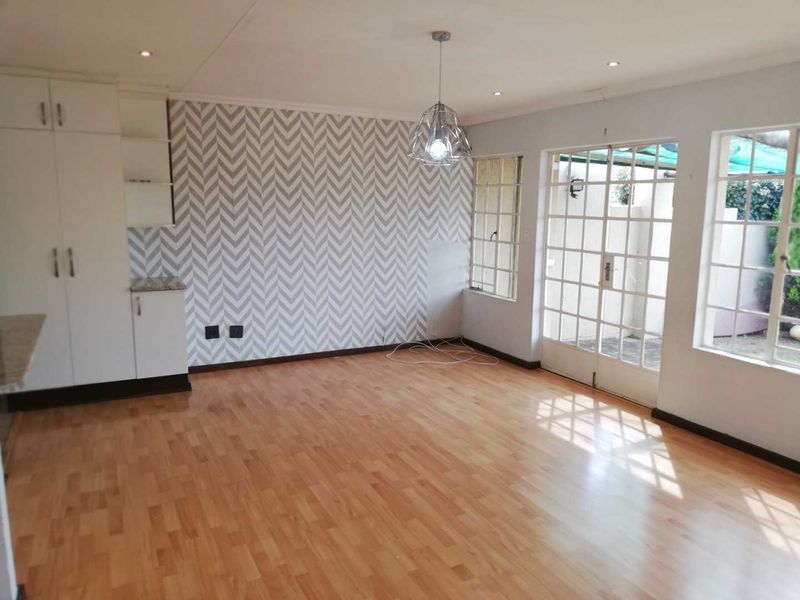 Spacious open-plan living area featuring laminate flooring, built-in cabinetry, and direct access to the outdoor area through classic french doors.