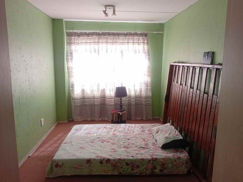A bedroom featuring green painted walls and a large window with a curtain rail, requiring cosmetic updates to improve the overall aesthetic.