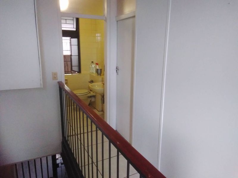 A view of a hallway featuring a metal balustrade and tiled flooring, leading directly into a functional bathroom space.