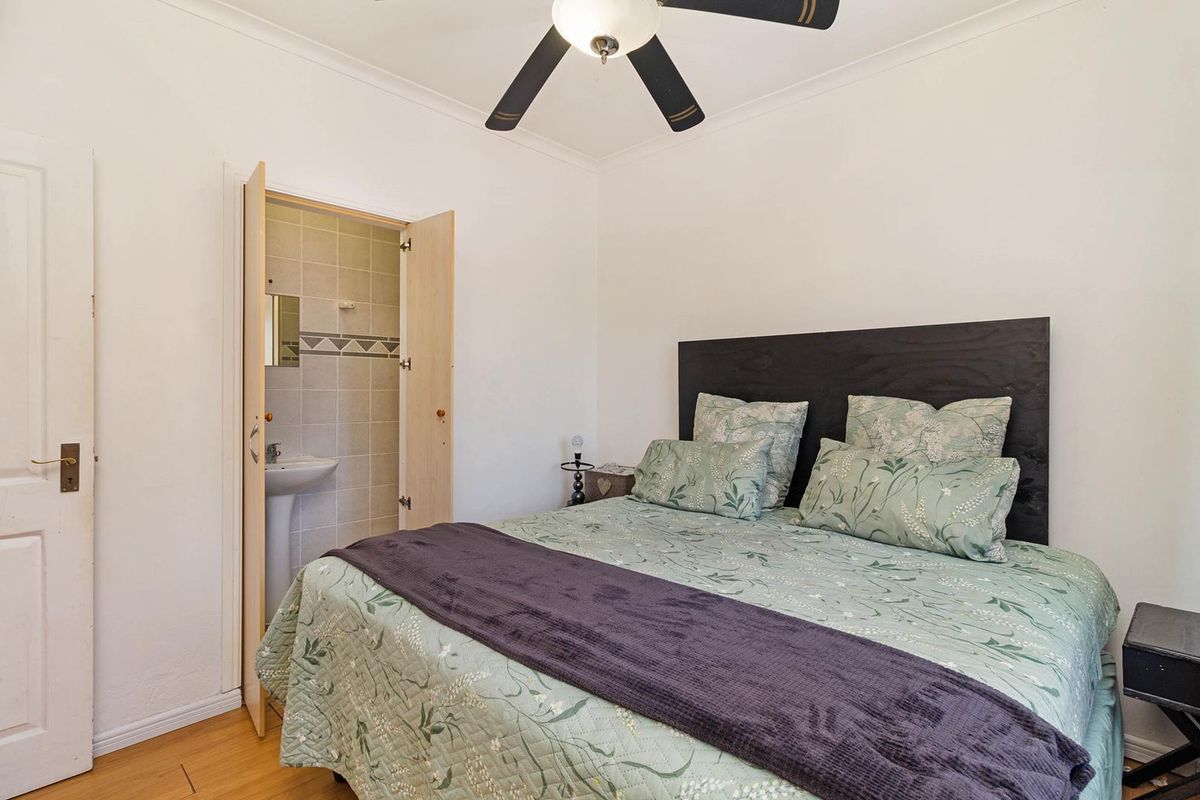 A bedroom featuring laminate flooring, a ceiling fan, and an en-suite bathroom with a pedestal basin.