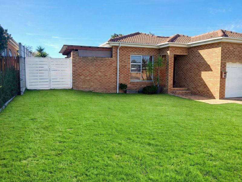 A well-maintained face brick house featuring a tiled roof, integrated garage, and a neat front lawn with a secure white gate.