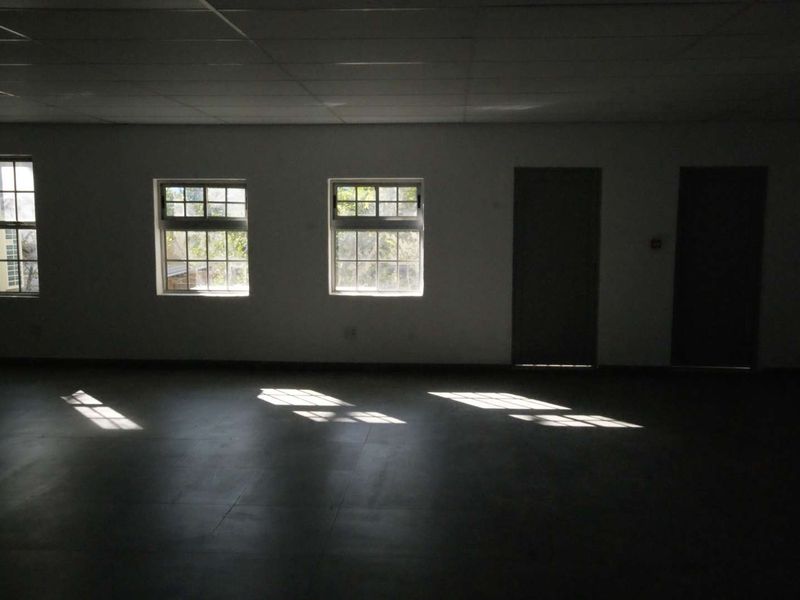 A spacious, empty office area featuring tiled flooring, a grid ceiling, and multiple windows providing natural light.