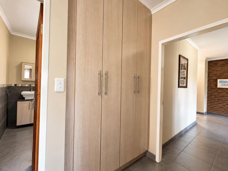 A clean, well-maintained hallway featuring neutral tiled flooring and ample built-in cupboard storage, providing a seamless transition between living areas.