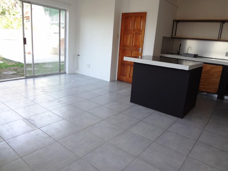 Open plan living area featuring tiled floors, a modern kitchen island, and a sliding glass door providing direct access to the rear garden.