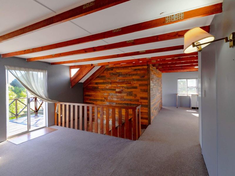 Spacious upper-level living area featuring exposed timber ceiling beams, rustic wood wall paneling, and direct access to an outdoor balcony.