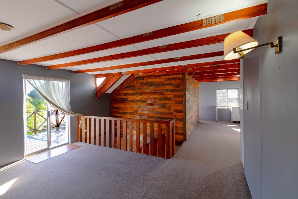 Spacious upper-level living area featuring exposed timber ceiling beams, rustic wood wall paneling, and direct access to an outdoor balcony.