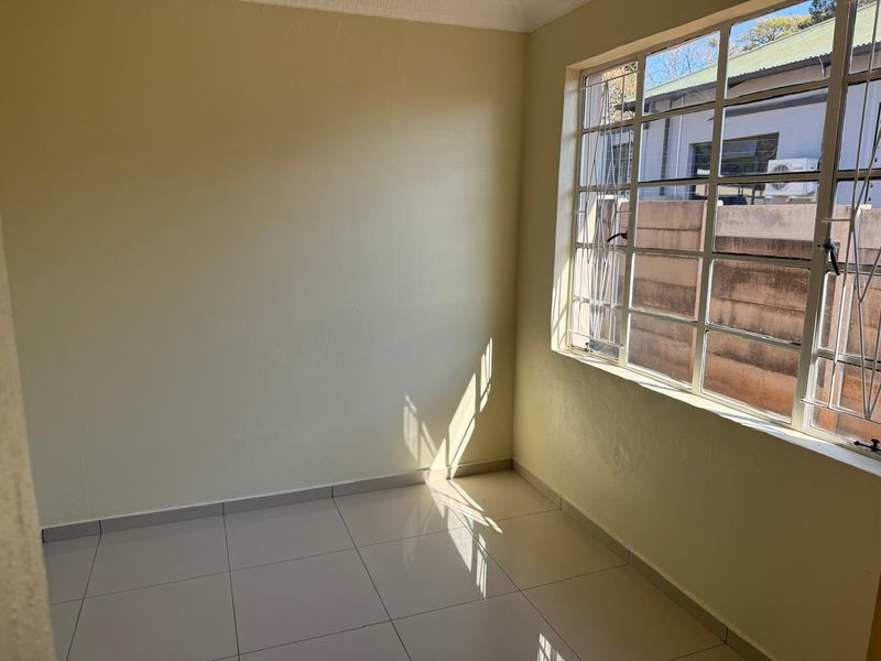 A bright, empty bedroom featuring neutral tiled flooring and a large steel-framed window with security bars, offering a clean canvas for personalization.