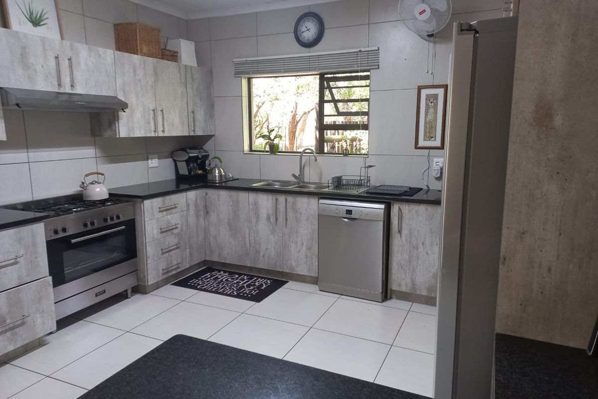 A functional kitchen featuring light wood-grain cabinetry, dark granite countertops, a stainless steel gas stove, and tiled flooring.