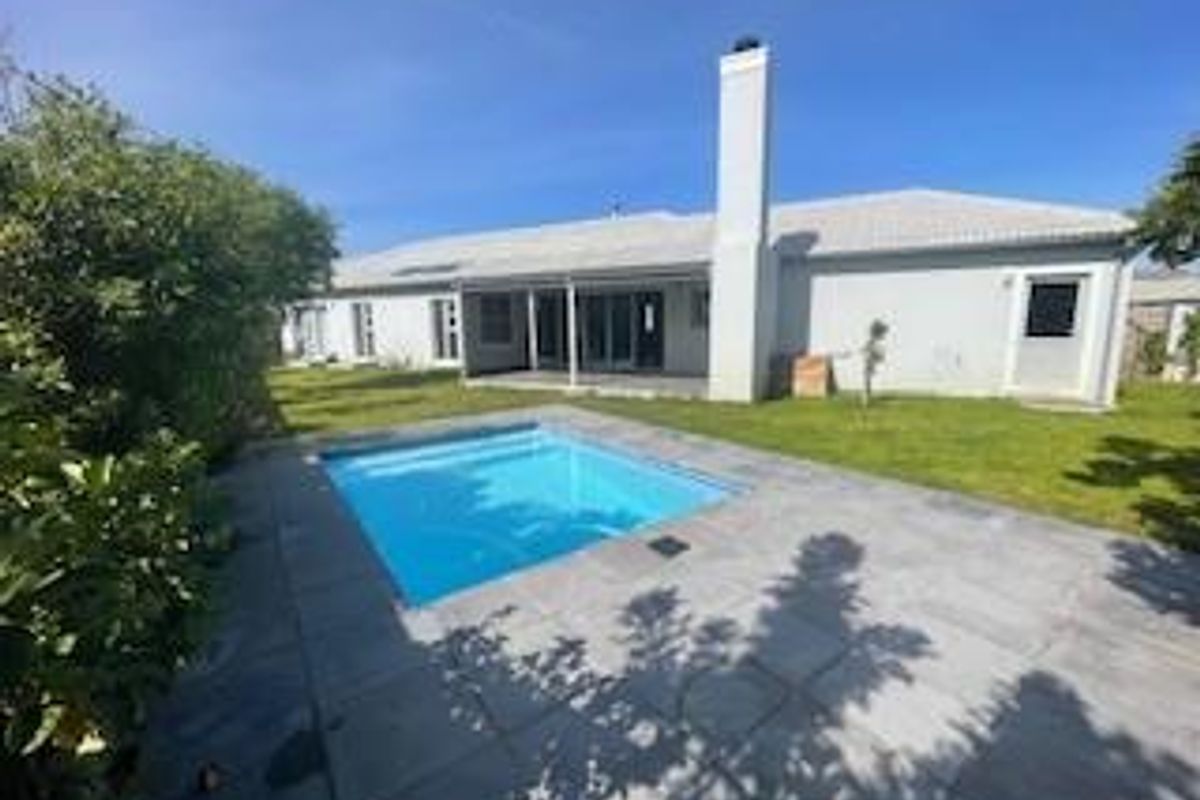 Rear exterior view of the house featuring a swimming pool, paved patio area, and a well-maintained lawn.