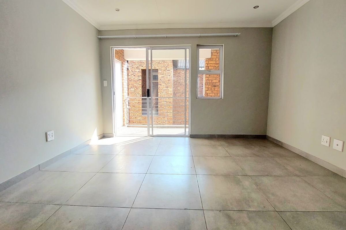 A bright, empty living area featuring large format floor tiles, recessed ceiling lighting, and sliding glass doors leading to a private balcony.