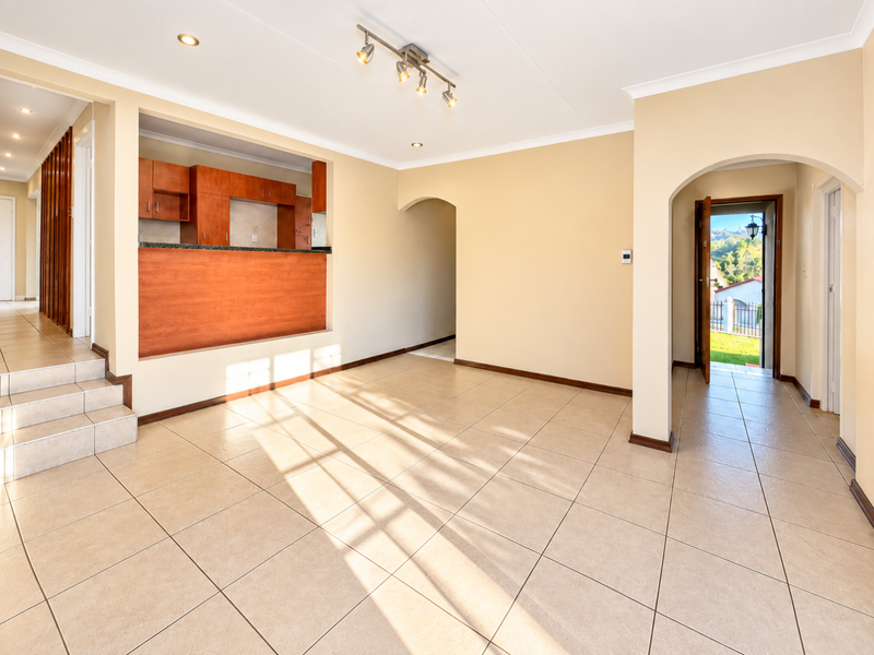 Spacious open-plan living area featuring neutral tiled flooring, recessed lighting, and a functional kitchen pass-through with built-in cabinetry.