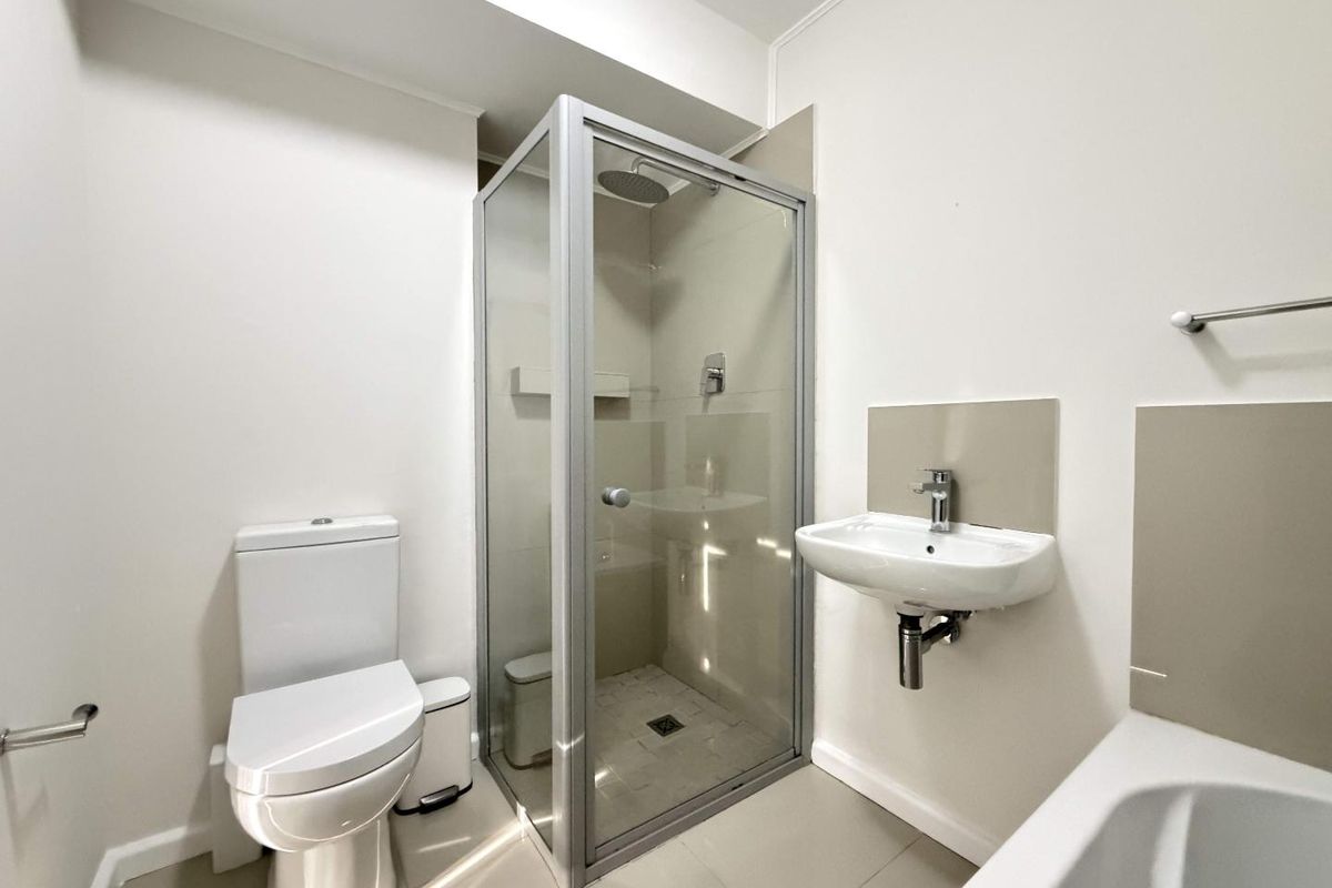 A clean, modern bathroom featuring a glass-enclosed shower, wall-mounted basin, and a white toilet with neutral floor and wall tiling.