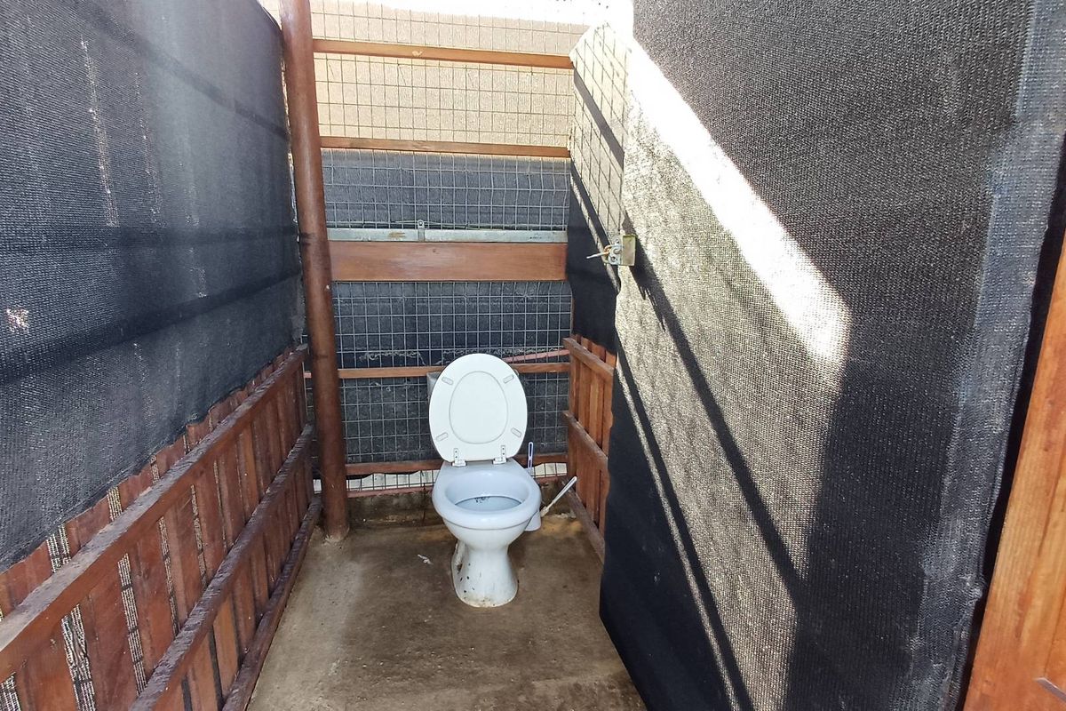 A basic outdoor-style bathroom facility featuring a toilet enclosed by temporary timber and mesh screening.