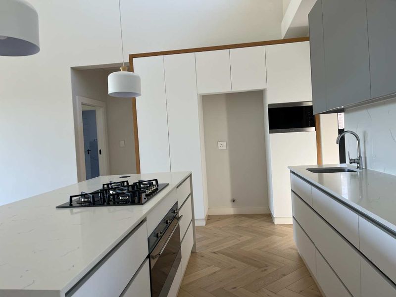 Modern kitchen featuring white cabinetry, quartz countertops, a central island with a gas hob, built-in oven, and elegant herringbone timber flooring.