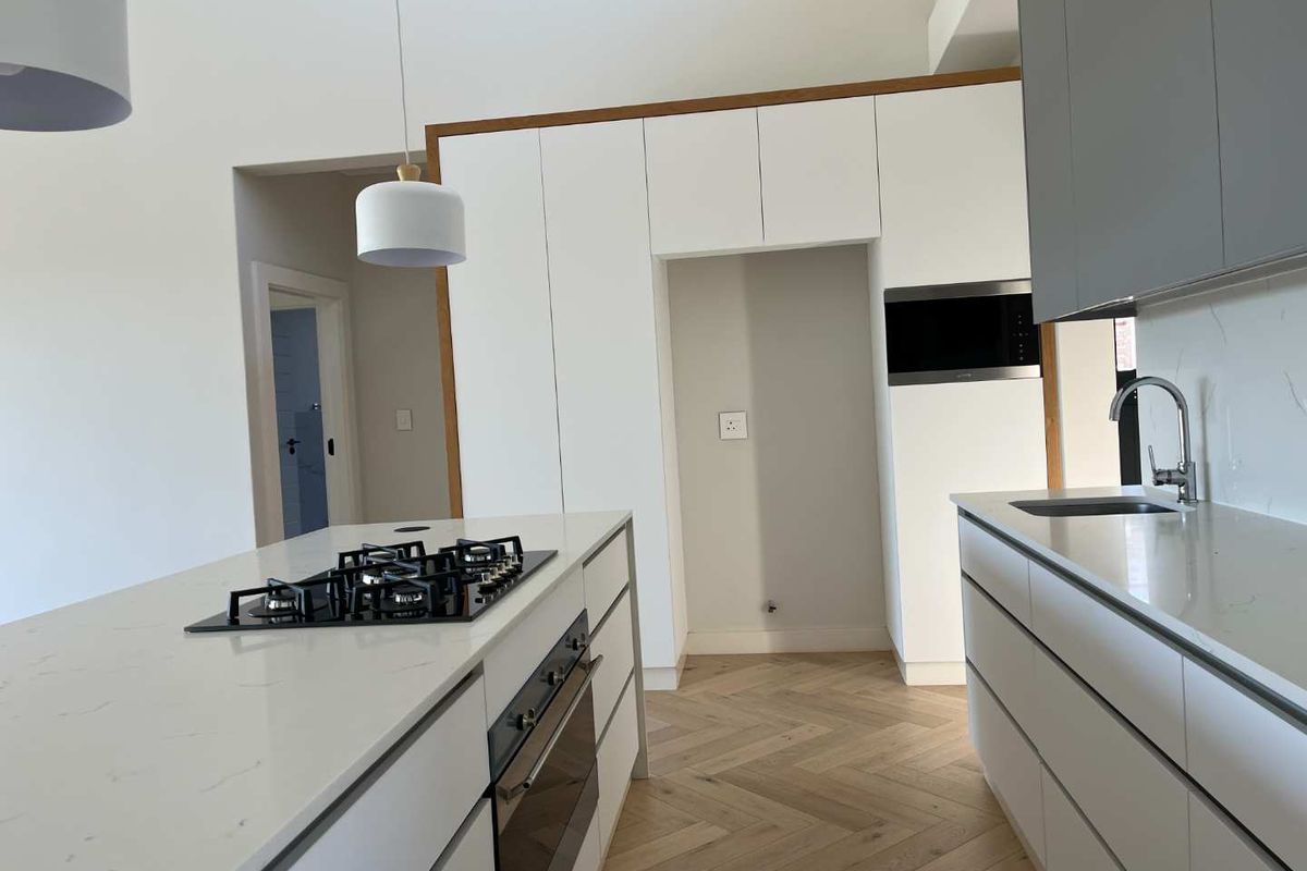 Modern kitchen featuring white cabinetry, quartz countertops, a central island with a gas hob, built-in oven, and elegant herringbone timber flooring.