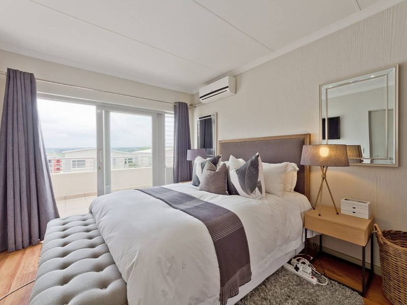 A well-maintained bedroom featuring laminate flooring, an air conditioning unit, and large sliding glass doors providing direct access to a private balcony.