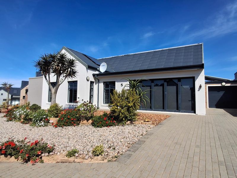 Modern single-story residence featuring a corrugated metal roof, paved driveway, integrated garage, and well-maintained landscaped front garden.