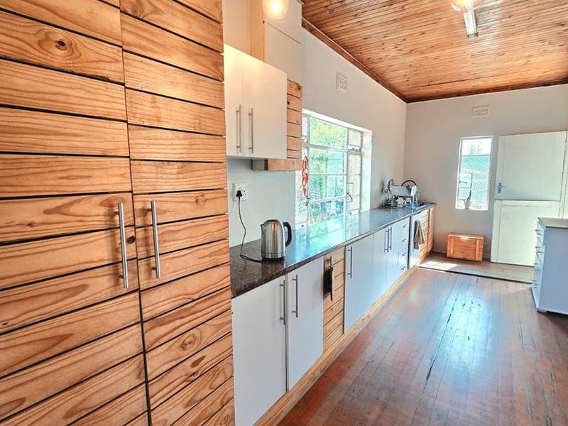A galley-style kitchen featuring warm timber ceilings, hardwood flooring, granite countertops, and a mix of natural wood and white cabinetry.