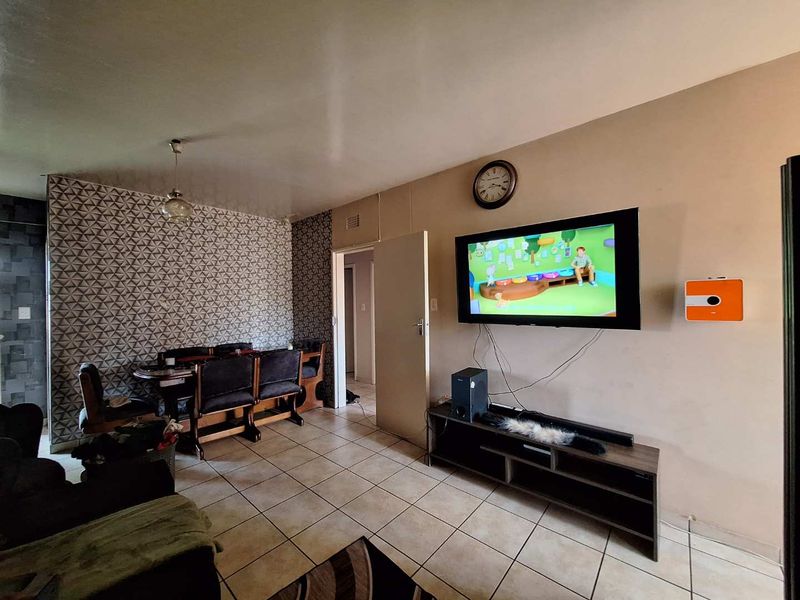Open plan living and dining area featuring tiled flooring, a decorative feature wall, and a wall-mounted television setup.