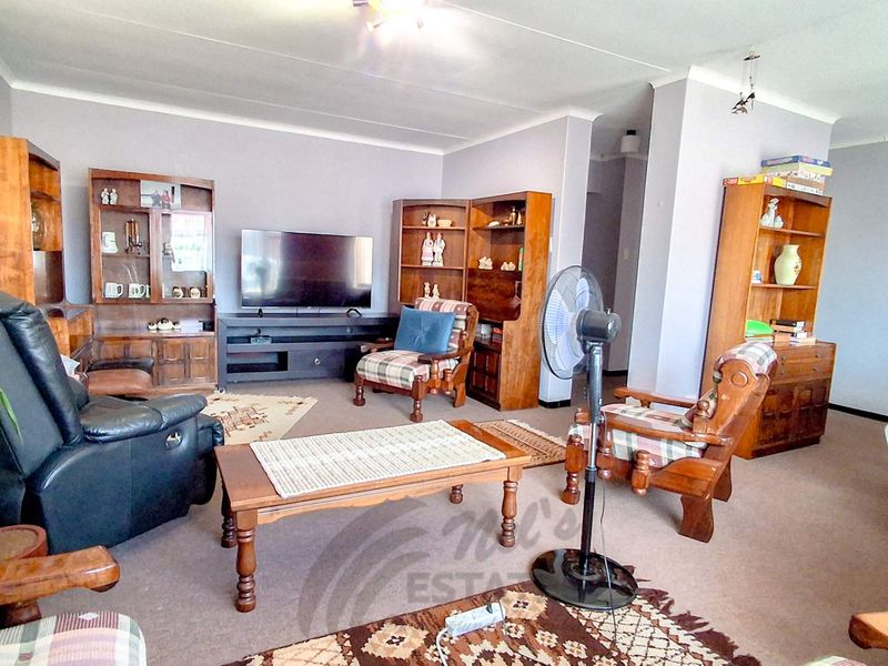 A spacious living room featuring neutral wall tones, coving, and carpeted flooring, offering a comfortable and functional layout for relaxation.