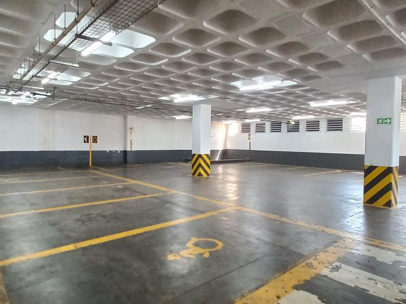 A spacious, well-lit underground parking garage featuring a waffle slab ceiling, concrete flooring with marked bays, and structural support columns.