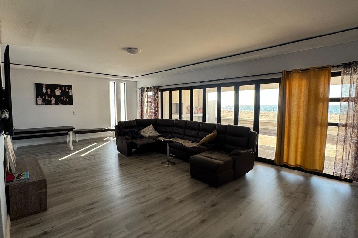 Spacious living room featuring modern laminate flooring and expansive sliding glass doors that provide seamless access to the outdoor area and ocean views.