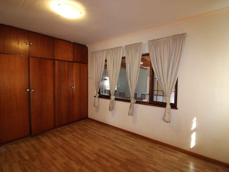 A spacious bedroom featuring wood-look laminate flooring and extensive floor-to-ceiling built-in wooden cupboards.