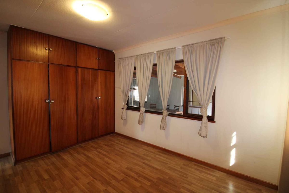 A spacious bedroom featuring wood-look laminate flooring and extensive floor-to-ceiling built-in wooden cupboards.