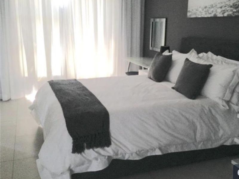 A well-lit bedroom featuring neutral tiled flooring and floor-to-ceiling sheer curtains, creating a bright and comfortable living space.