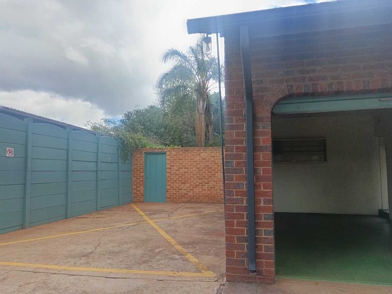 Exterior view of a brick garage structure with an adjacent paved driveway area and boundary walling.