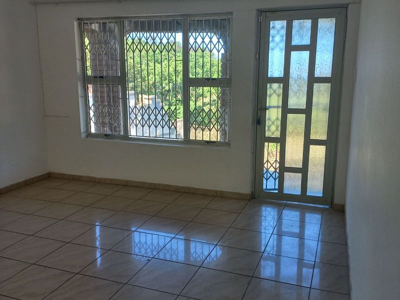 An empty living area featuring neutral tiled flooring, a glass panel door, and security bars on the windows, offering a clean, blank canvas.